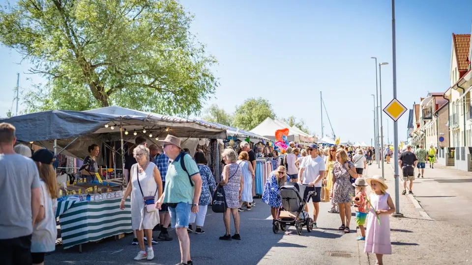 Folk strosar på marknad i en somrig härlig stadsmiljö.