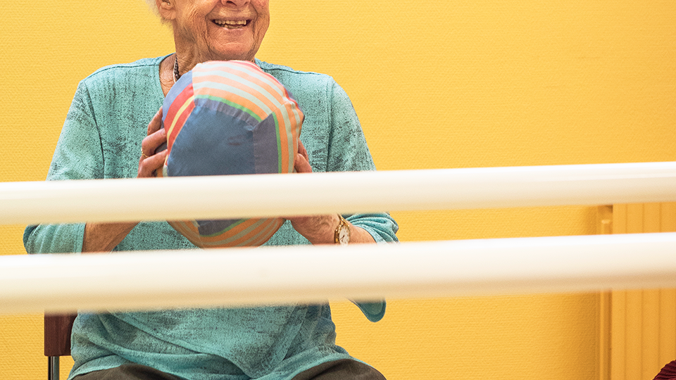En äldre kvinna klädd i turkos blus håller i en boll