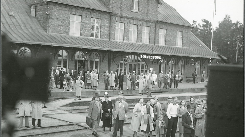 Gammalt svartvitt foto från Sölvesborgs järnvägsstation. Människor står på perrongen.
