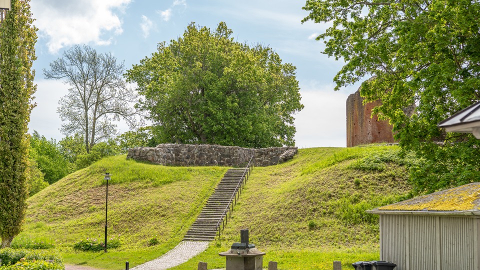 Slottsruinen skymtas uppe på en hög kulle en solig sommardag.