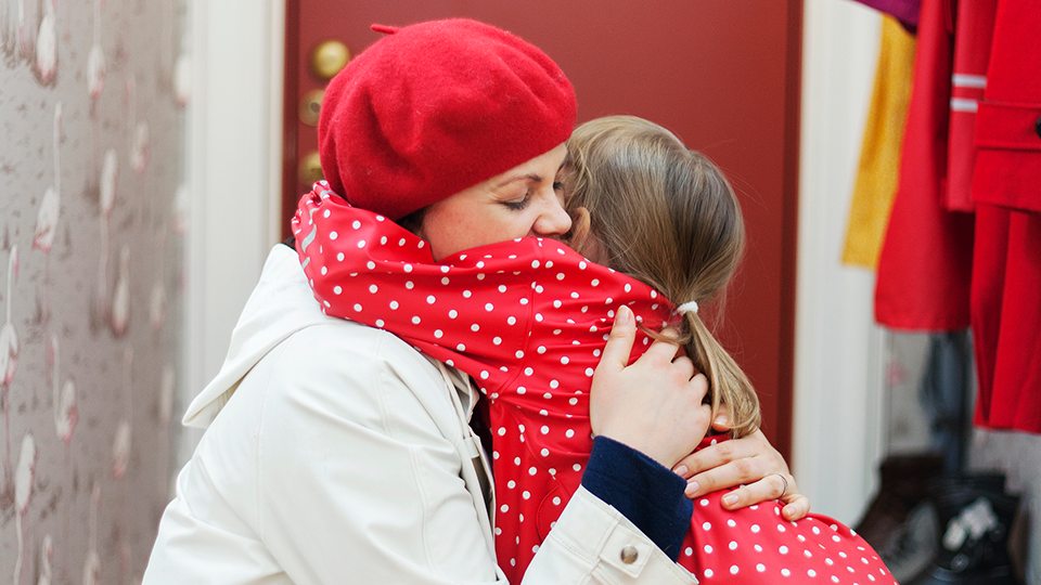En mamma kramar sin dotter hårt och kärleksfullt när de står vid dörren i en lägenhet