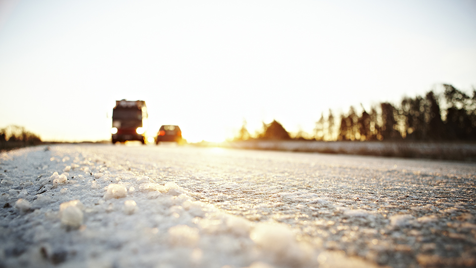 En väg med snö och en lastbil och en personbil i mjukt ljus.