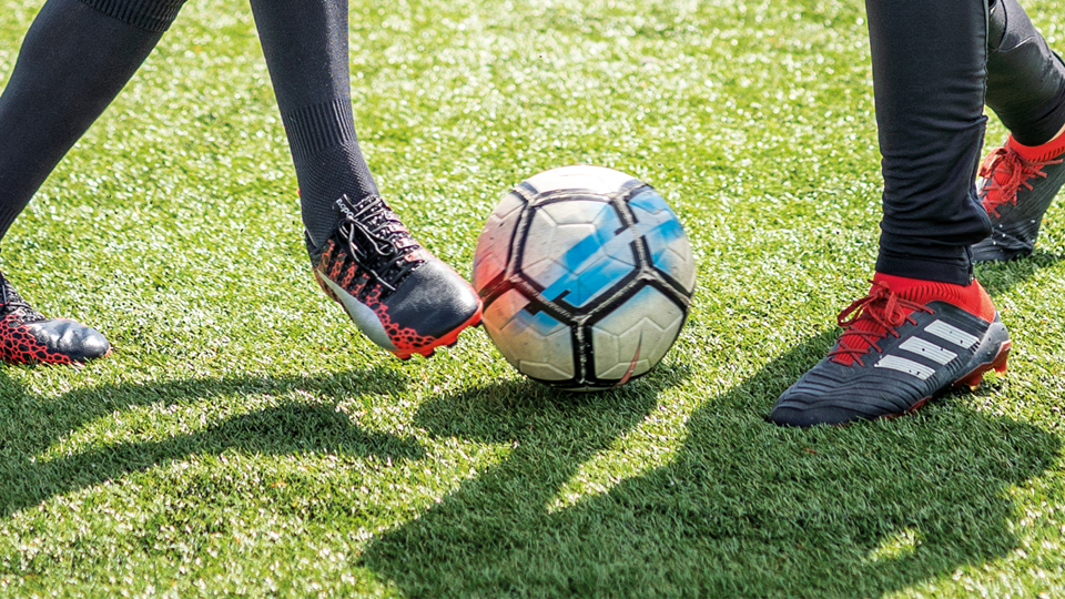 Fotbollsskor och en fotboll på gräsplan.