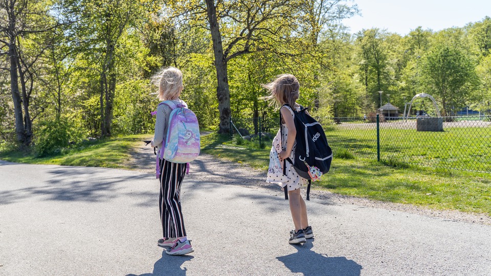Två flickor är på väg mot skolan med varsin skolväska på ryggen