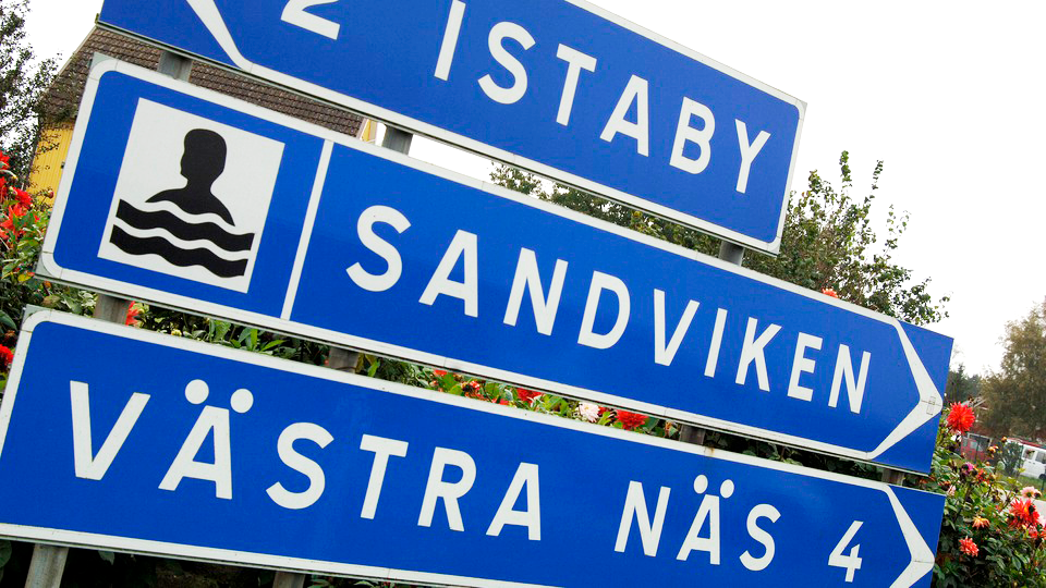 Blå vägskylt som pekar mot Sandviken och en ikon som illustrerar en badplats.