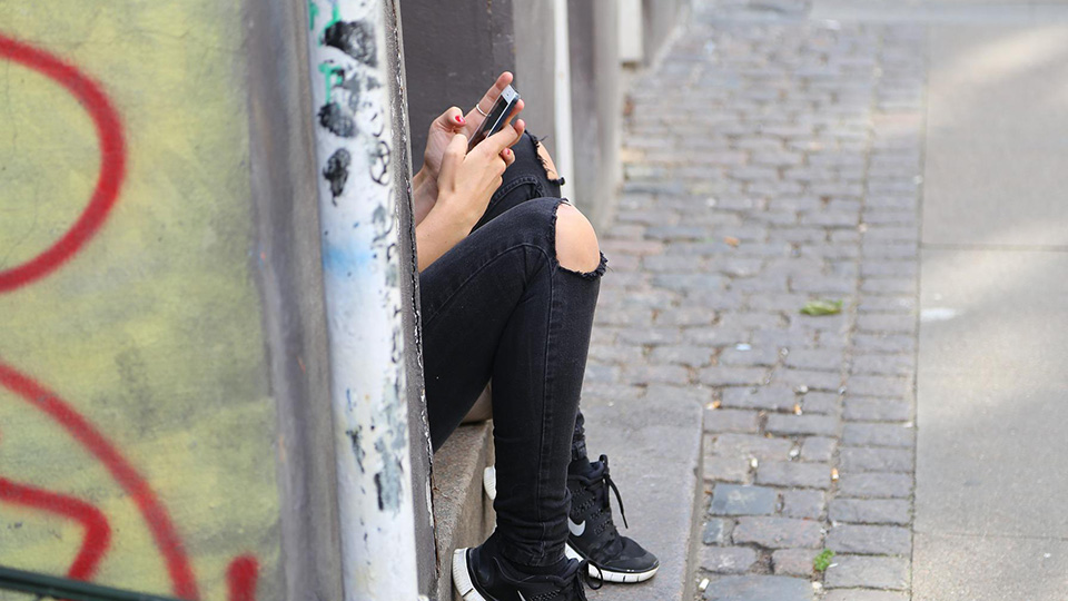 En tjej sitter på en trappa och kollar i sin mobil.