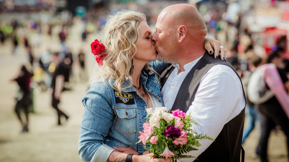 Ett par pussas på festivalområdet och bruden håller i en brudbukett