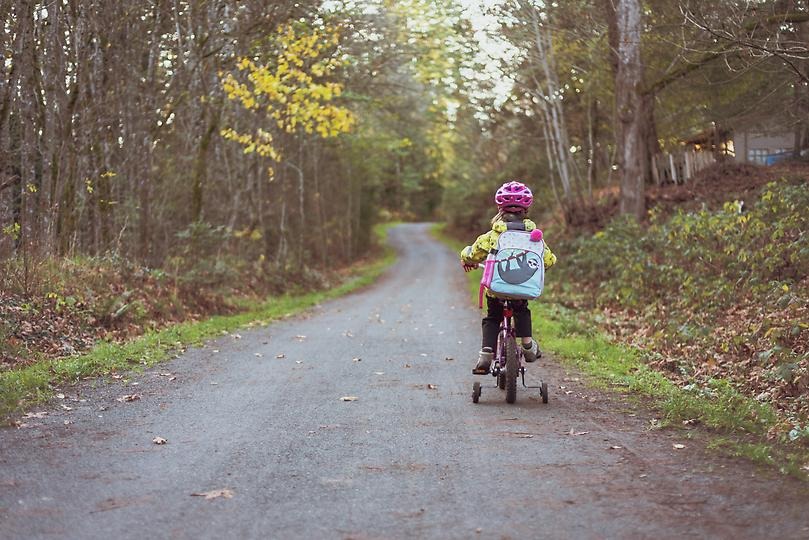 Liten tjej i cykelhjälm cyklar på skogsväg