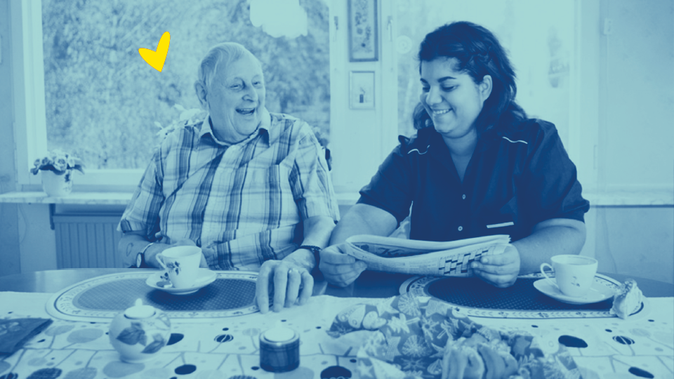 Blå duoton över äldre man och hemtjänstpersonal som läser tidning vid köksbordet.