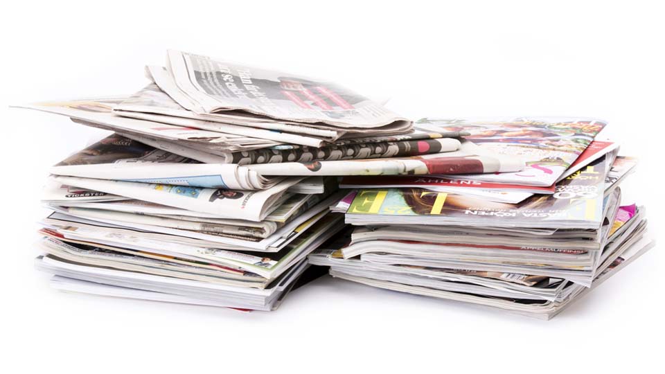 Två travar med dagstidningar och magasin redo att återvinnas.