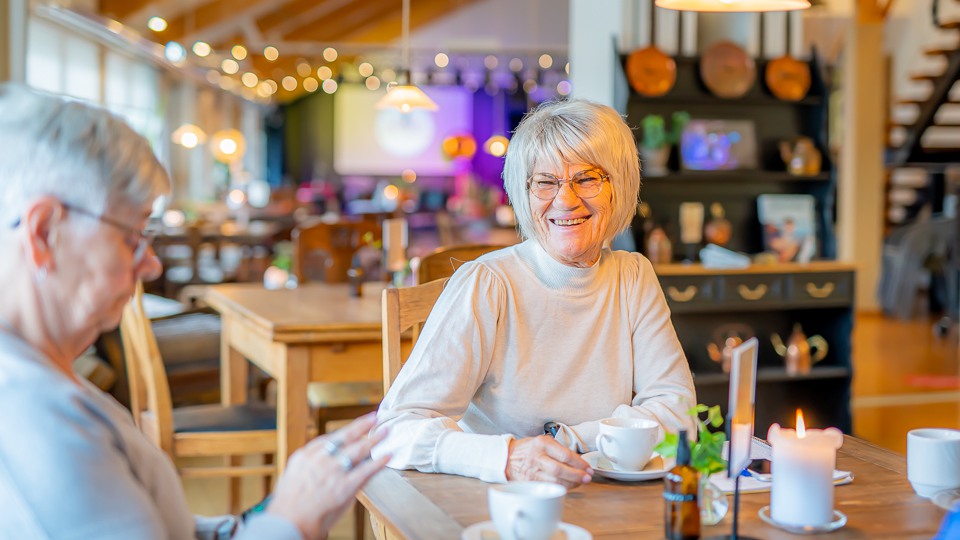 En leendes kvinna dricker kaffe med en vän på Duvans café.