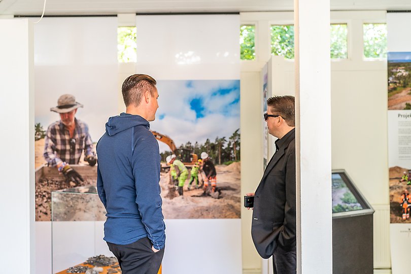 Två män inspekterar en utställning med bilder av en arkeologiska utgrävning.