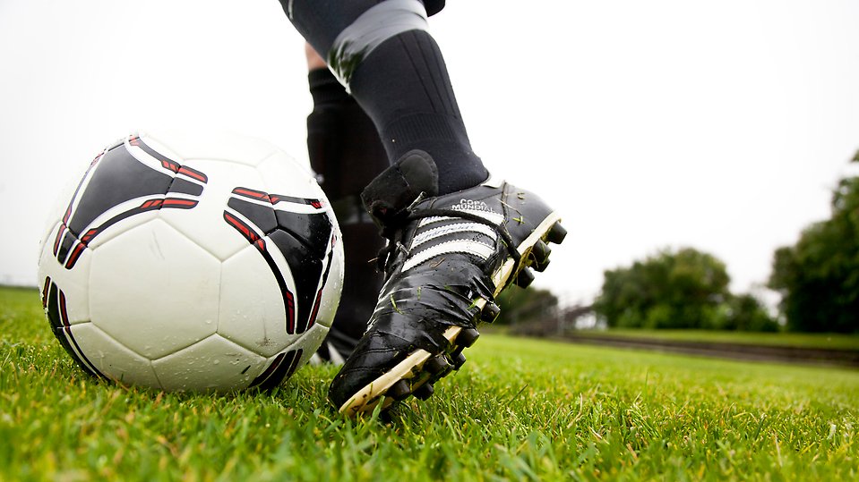 Fotbollssko touchar en fotboll på en gräsplan