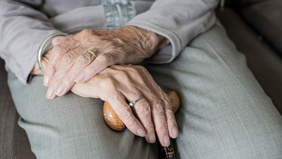 Bilden visar en äldre kvinnas händer och en käpp