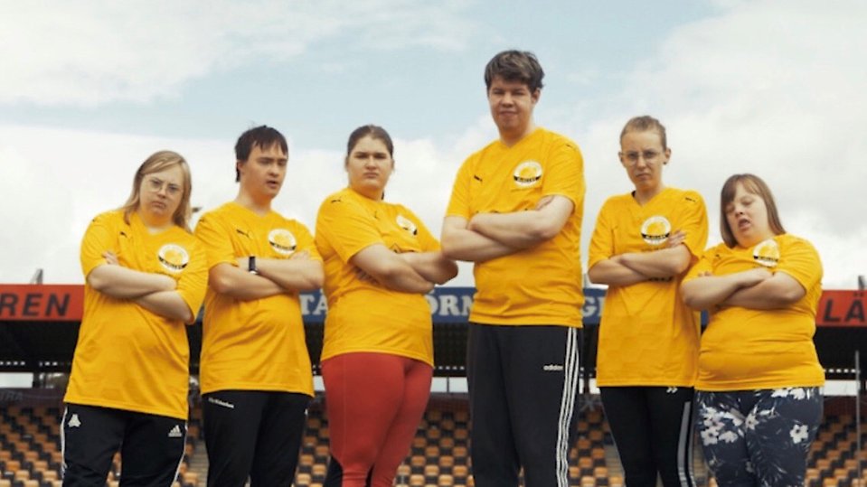 Står sex personer med funktionsvariation med händerna i kors på en fotbollsplan