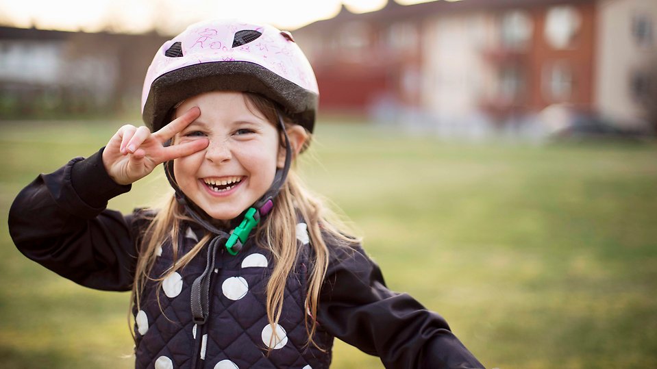 En tjej håller sin hand framför ena ögat och gör ett v-tecken. På huvudet har hon en cykelhjälm med grönt spänne. foto: Emma Bourne, Scandinav bildbyrå 