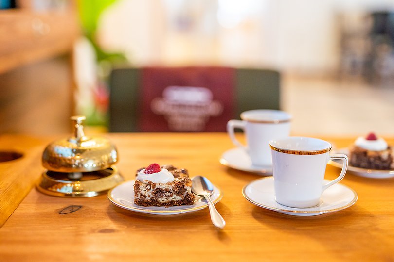 Två koppar kaffe och kaka står på ett bord intill gammeldags ringklocka