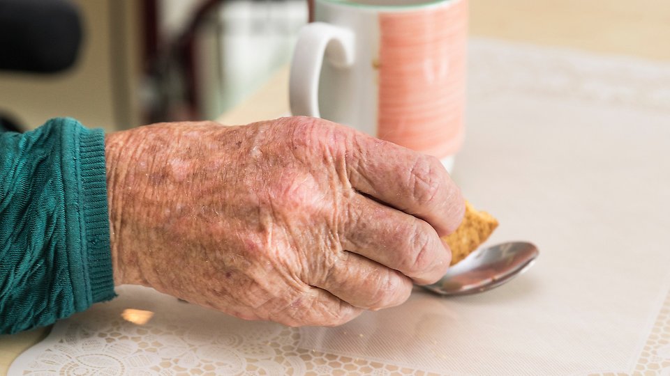 Bilden visar en gammal persons hand och en kaffekopp